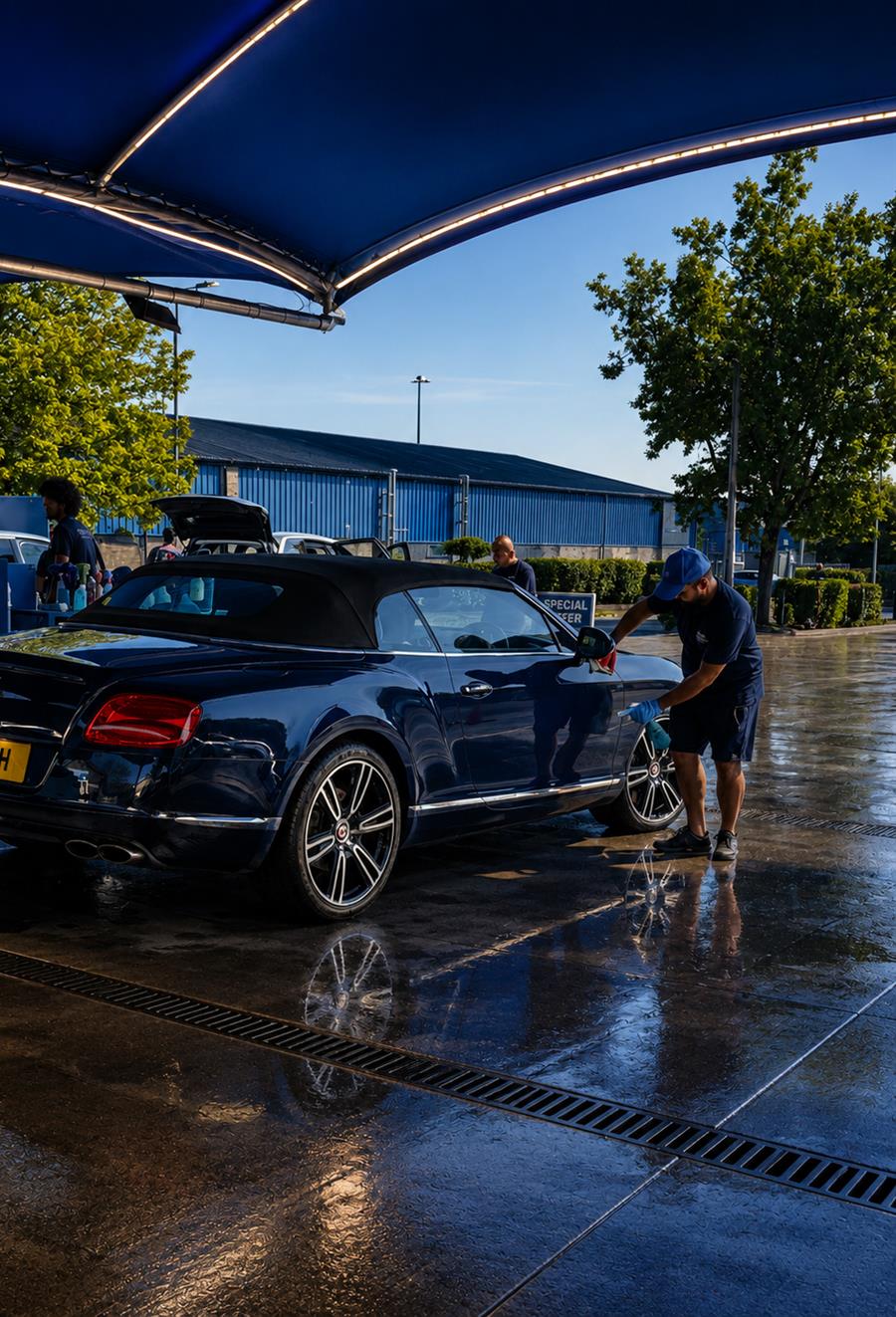 A Bentley convertible being polished by hand under the lit wash canopy