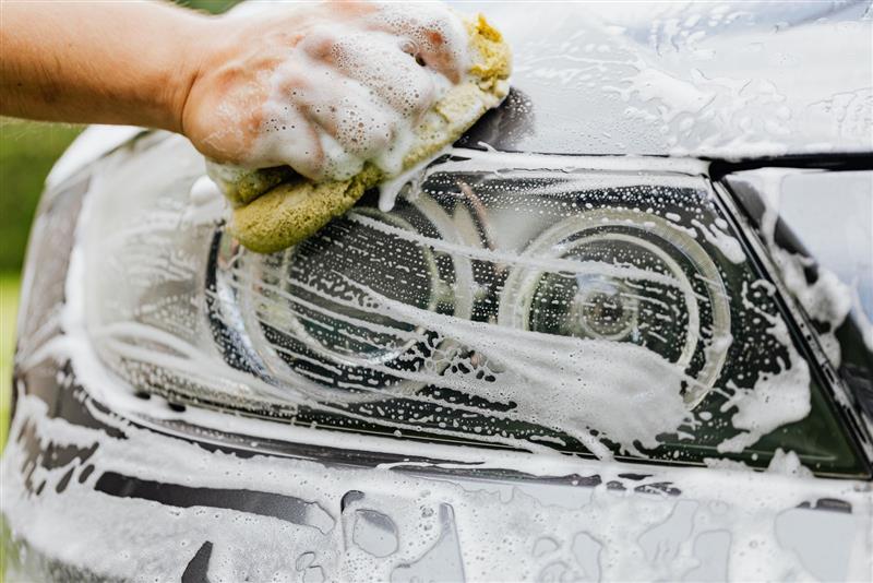 A headlight being washed by hand with a sponge and foam